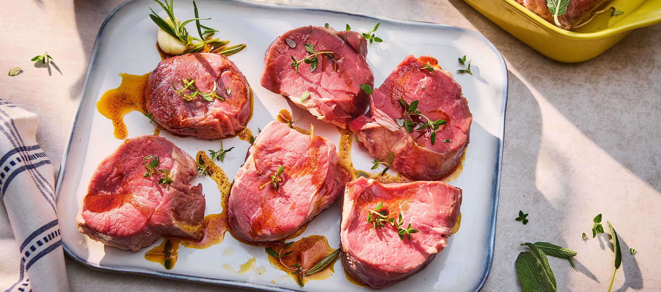 Fresh beef steaks with herbs and oil on a white platter.