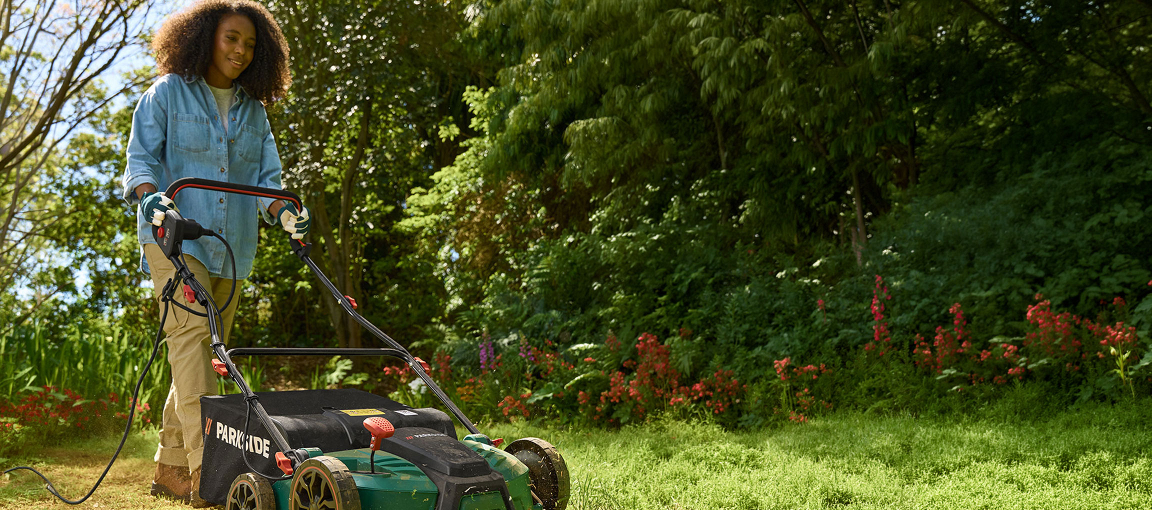 Woman in a garden using an electric lawnmower to cut grass.