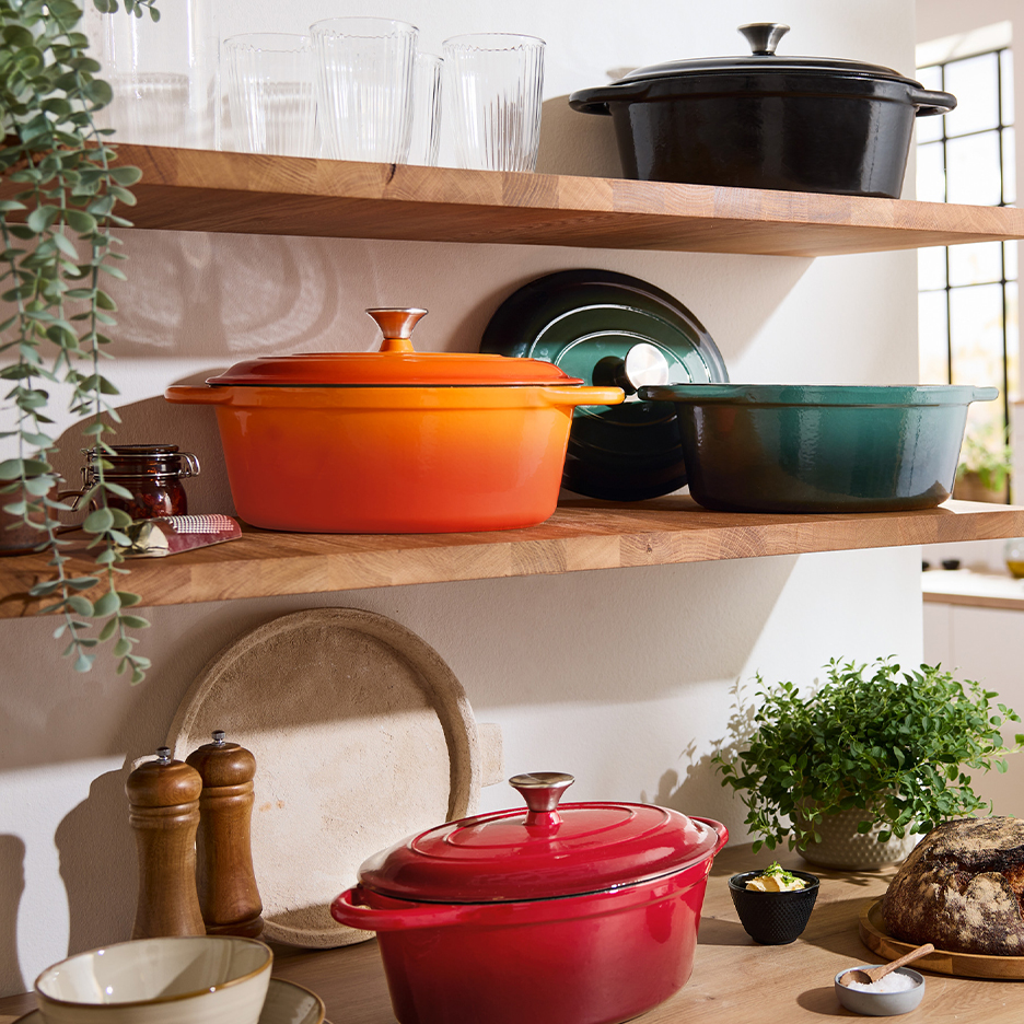 Colorful cast iron pots on wooden shelves in a bright kitchen.