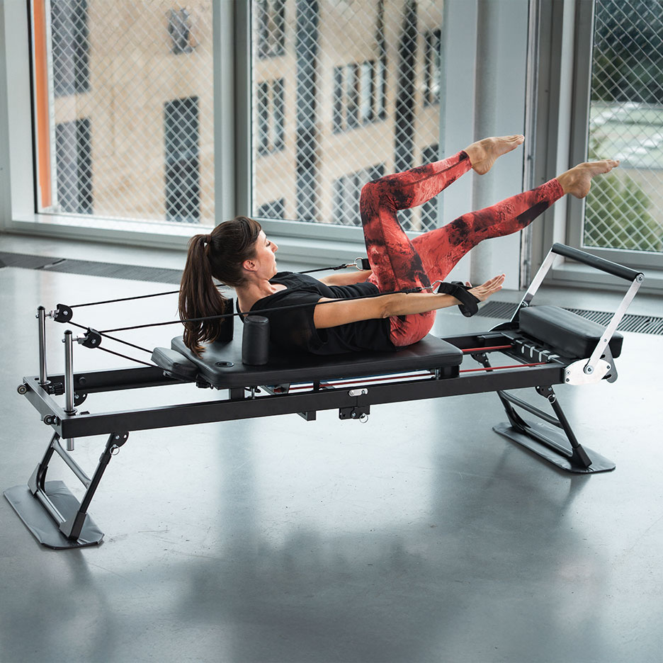 Woman doing Pilates exercise on a reformer with red yoga pants.