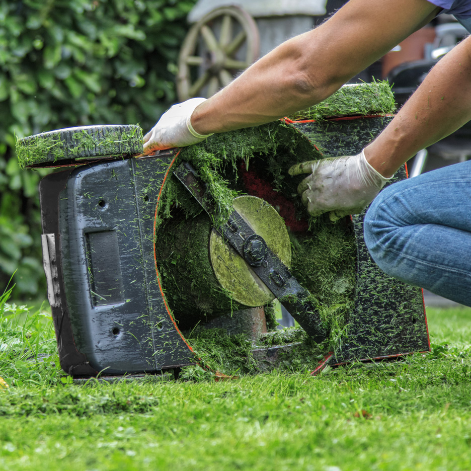 Person cleaning the lawnmower blade from grass.