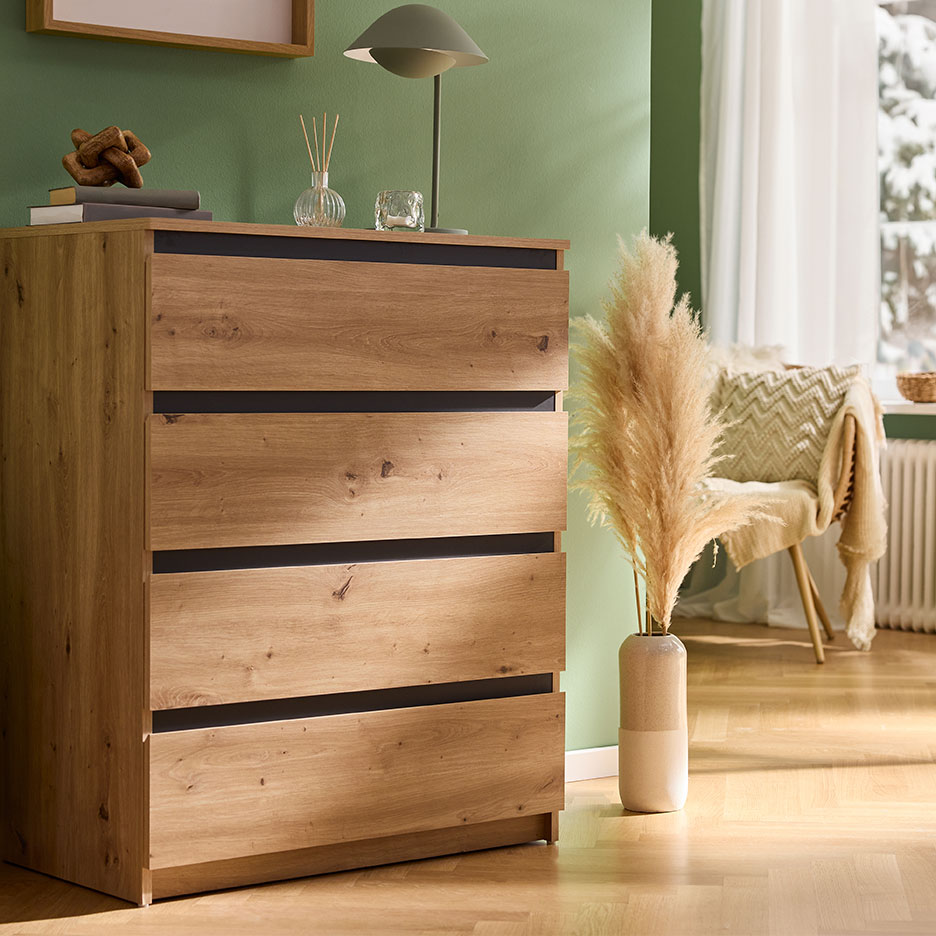 Wooden four-drawer chest, decorated with a lamp and a vase with pampas grass in a green room.