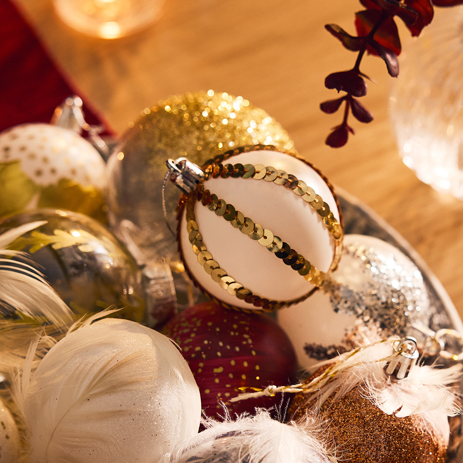 A bowl of gold, white, and red Christmas baubles, with feathers and sequins.