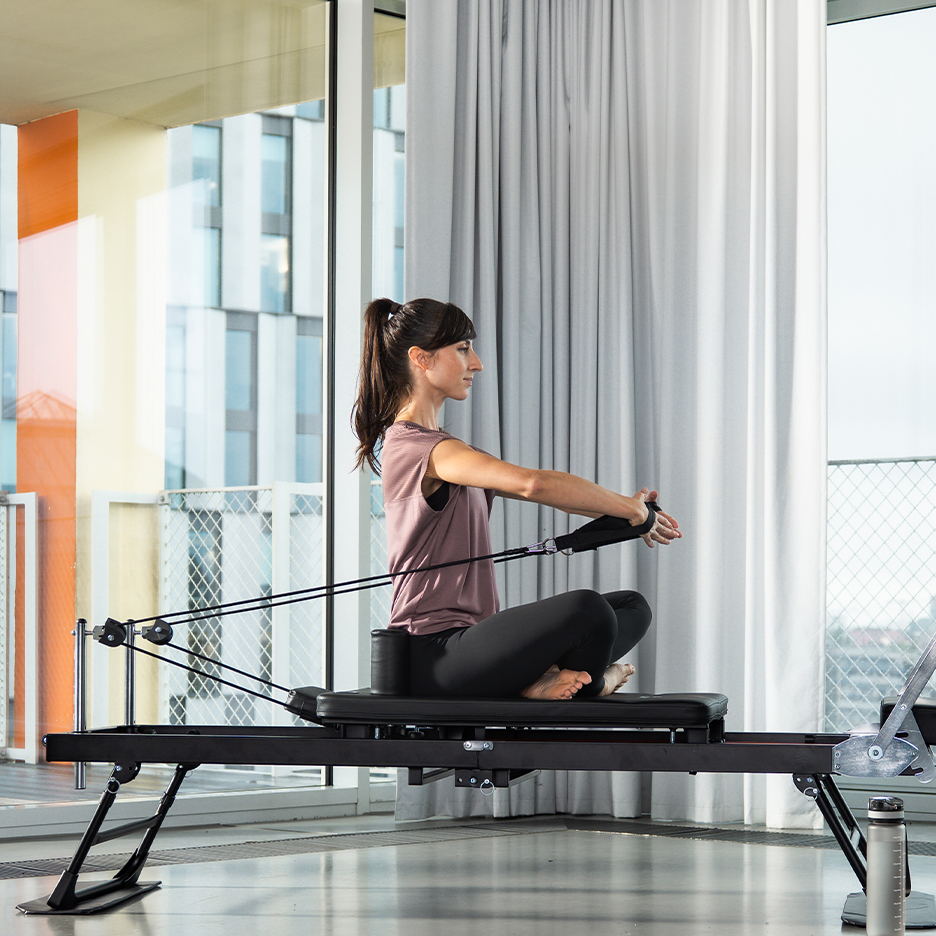 Woman doing Pilates on a reformer with resistance bands, in a modern interior.