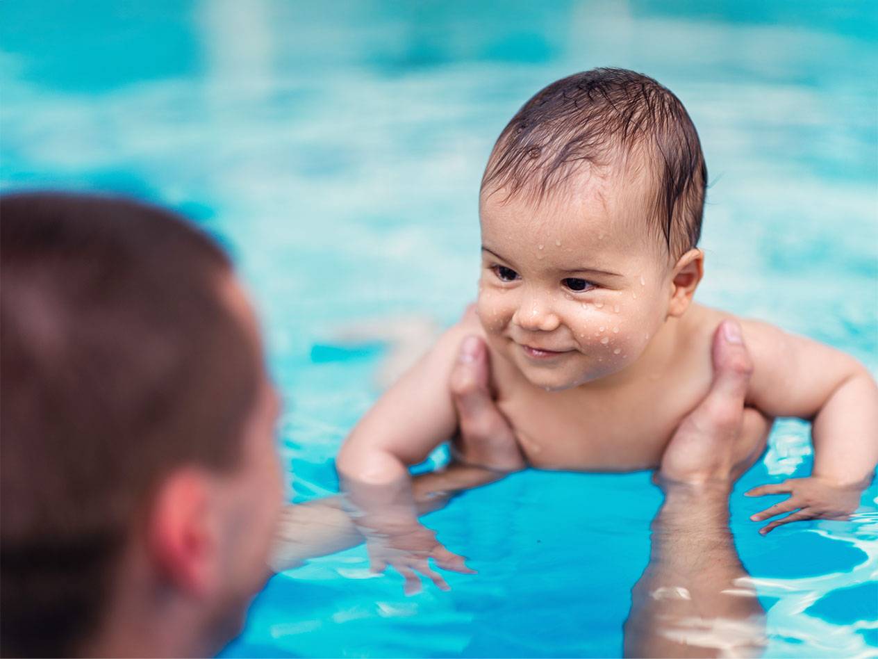 Baby swimming in a pool with an adult.