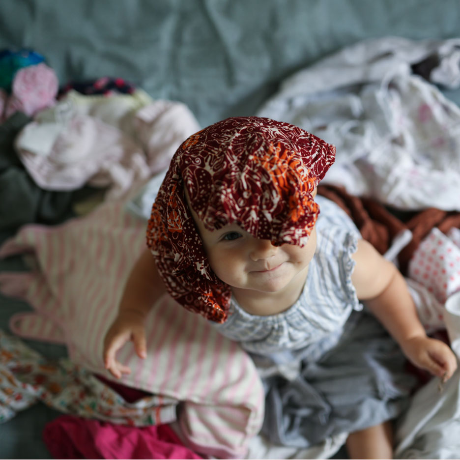 Baby with headscarf surrounded by clothes.