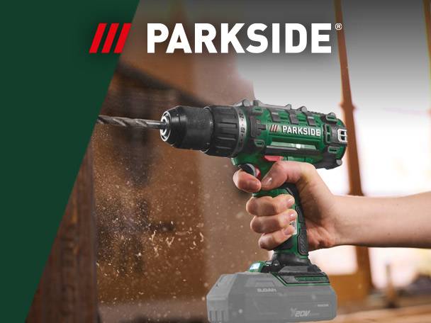A cordless drill in action, drilling into wood, with wood shavings flying.