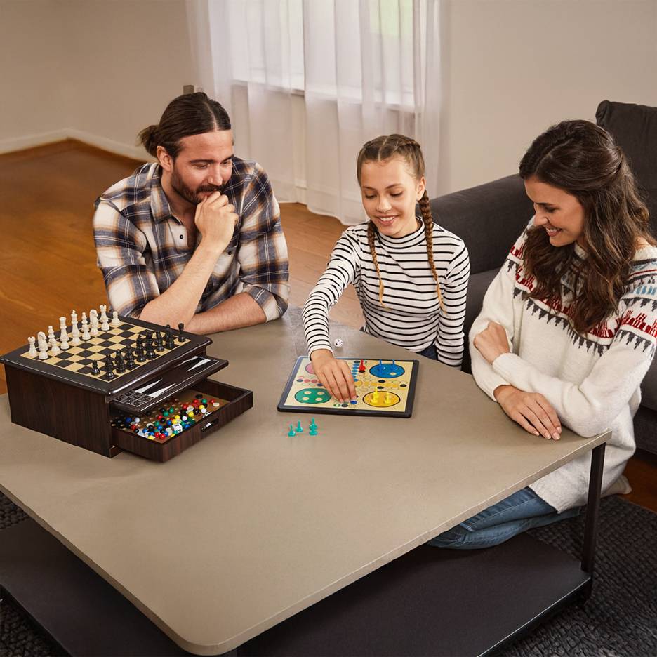 Family playing board games, including chess and Ludo, on a coffee table.