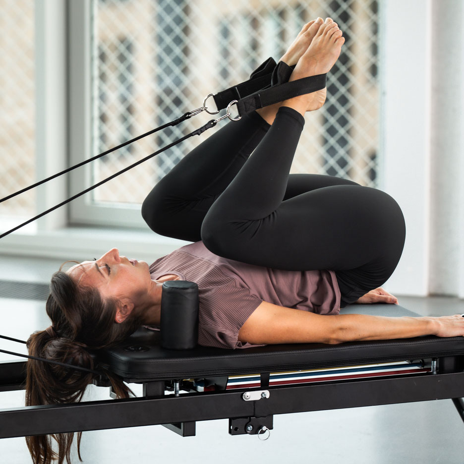 Woman exercising Pilates on a reformer with her legs in straps.