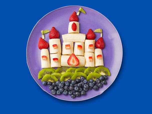 Fruit castle made of bananas, strawberries, kiwi, and blueberries.