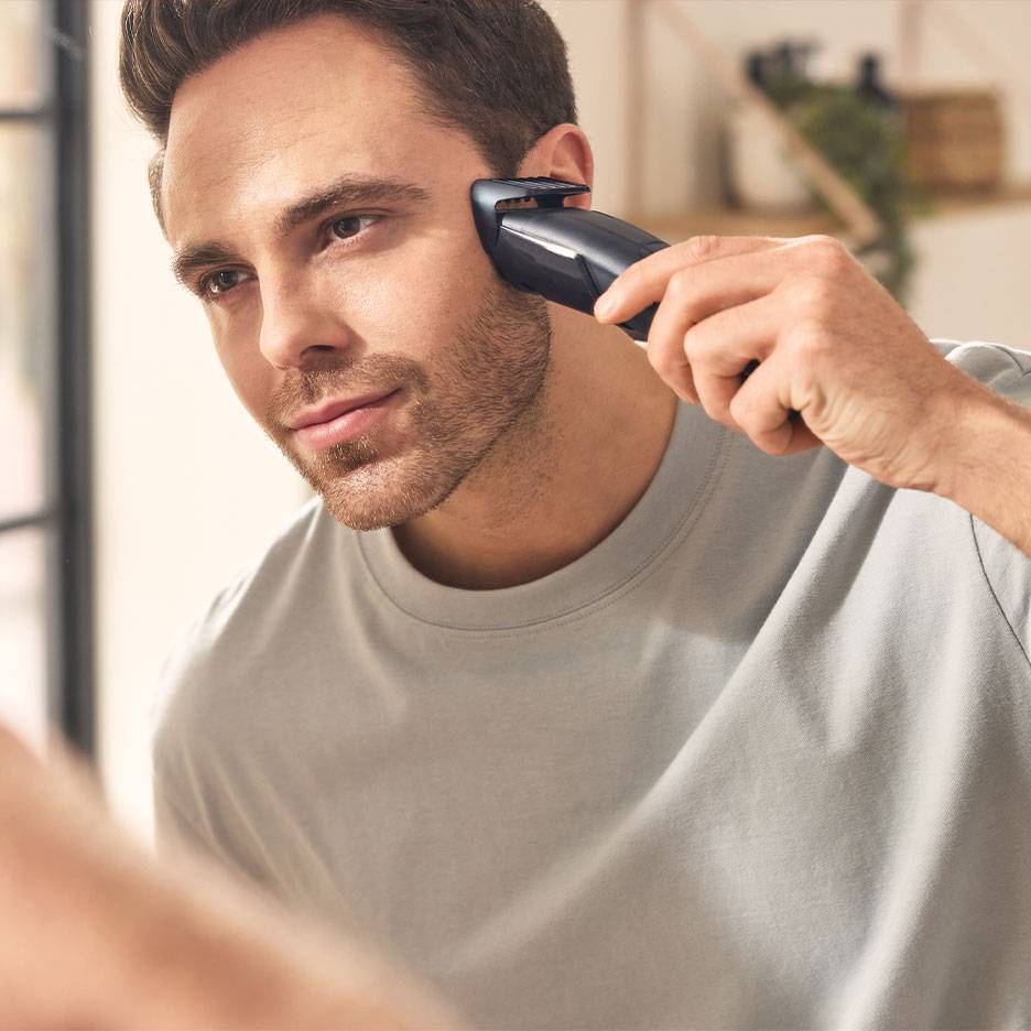 Man trimming his beard with a beard trimmer in front of a mirror.