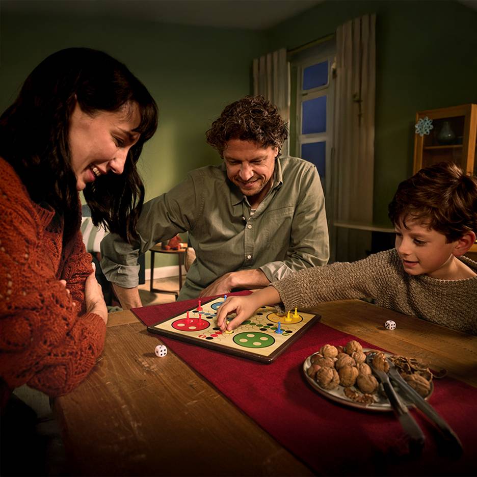 A family plays a board game with walnuts and two dice on a table.