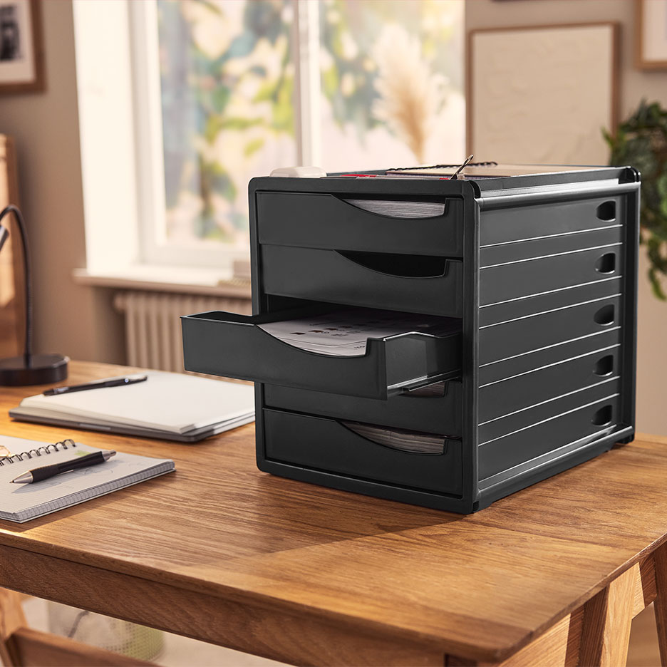 Black desk organizer with drawers, filled with papers, on a wooden table