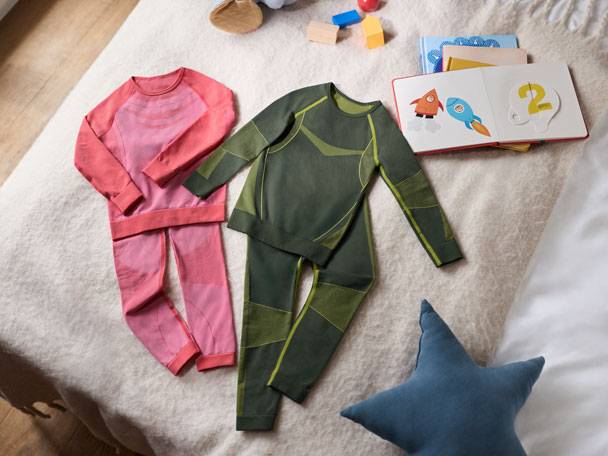 Two sets of children's thermal underwear (pink and green) and a book on a bed.