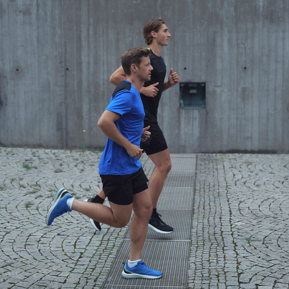 Two men in sportswear running outdoors on a cobblestone street.