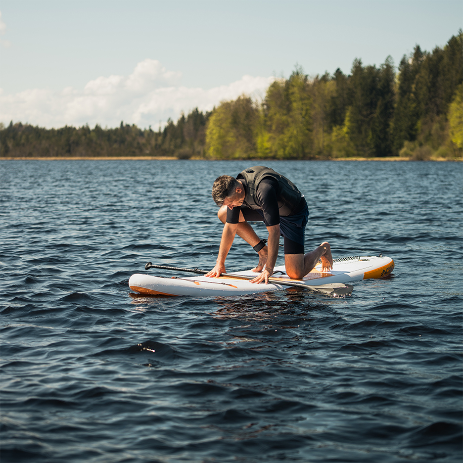 Man kneeling on a paddleboard on a lake.