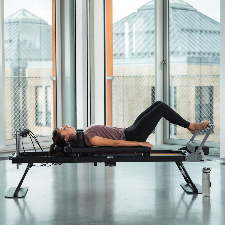 Woman doing Pilates on a reformer machine, with a water bottle beside it.