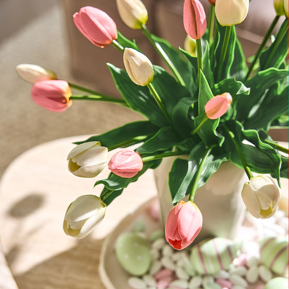 Vase of pink and white tulips with Easter eggs and sweets on a side table.