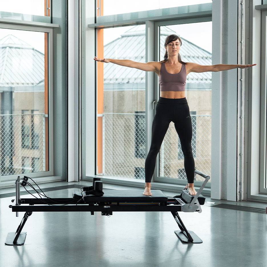 Woman doing Pilates on a reformer, with arms extended.