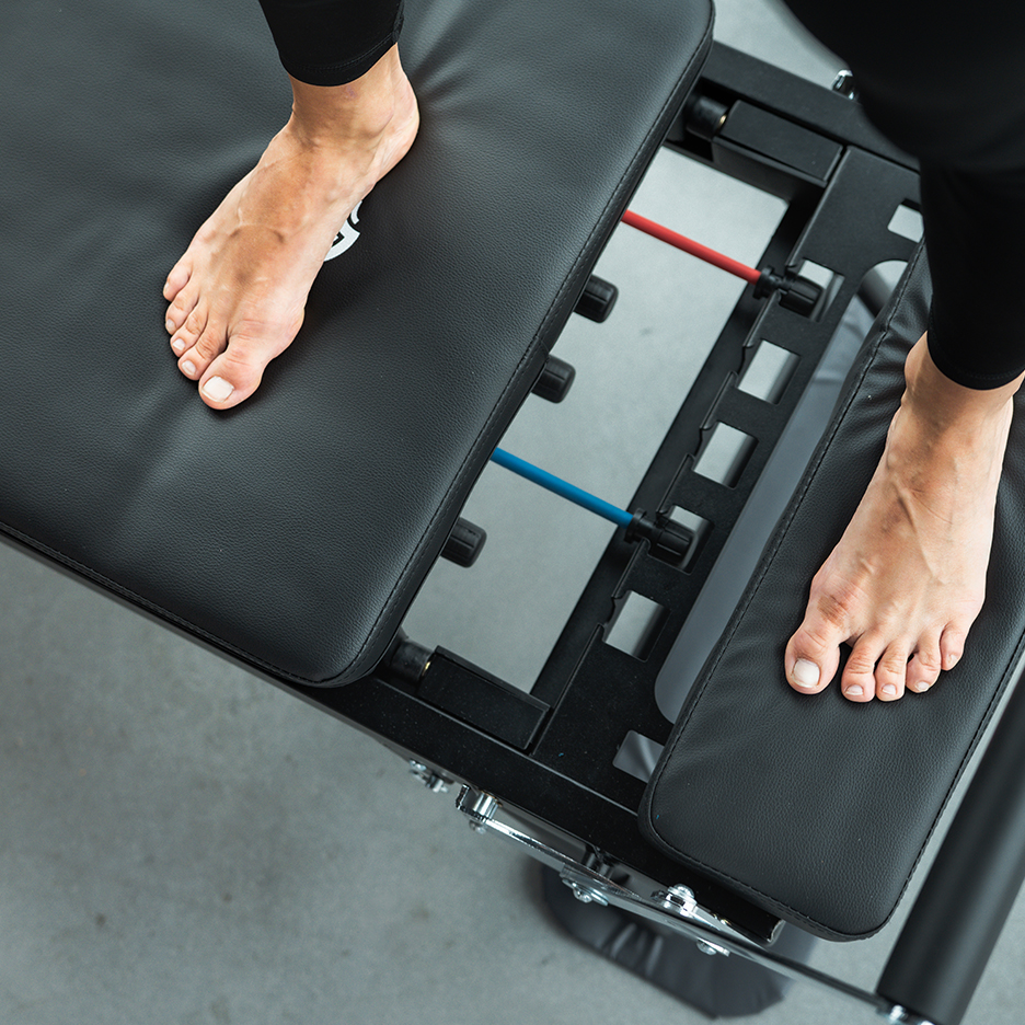 Bare feet on a black exercise bench with red and blue resistance bands.