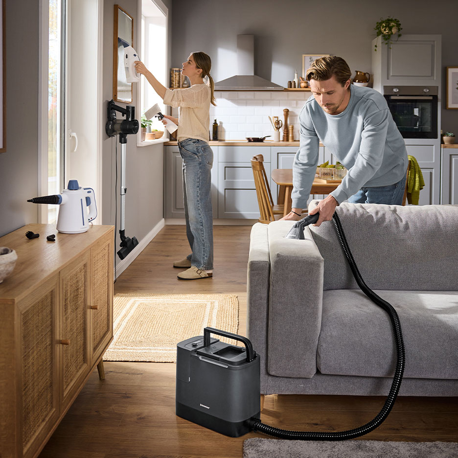 Man and woman cleaning home with a carpet cleaner and a handheld steam cleaner.