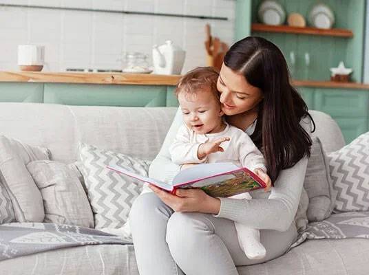 Mother reading a book to her toddler on a couch.