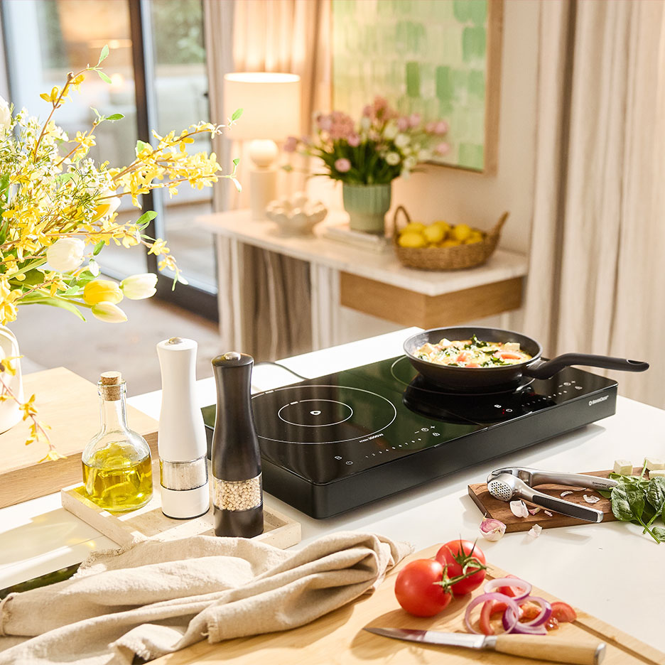 Induction hob with a pan, fresh vegetables and flowers in a bright kitchen.