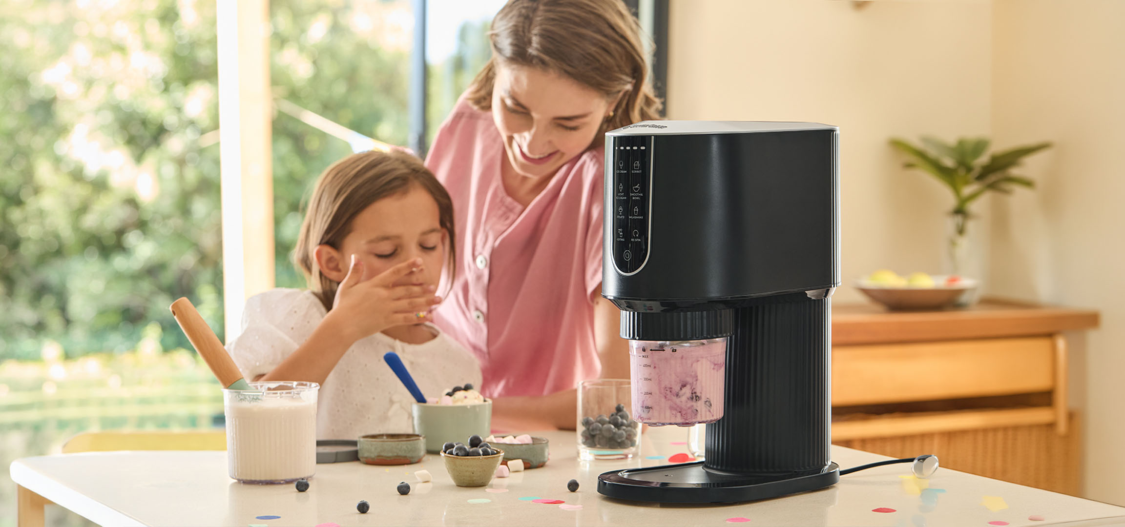 Woman and girl making desserts with an ice cream maker, surrounded by blueberries.