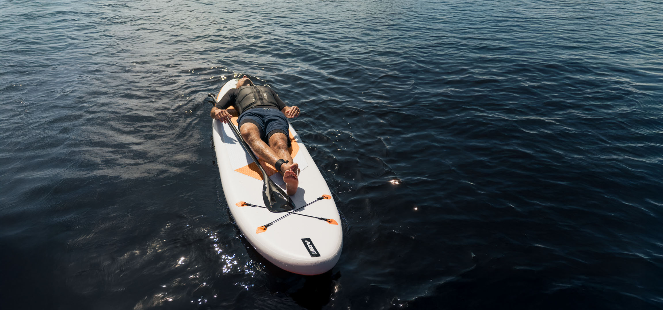 Man relaxing on a stand-up paddleboard in calm water.
