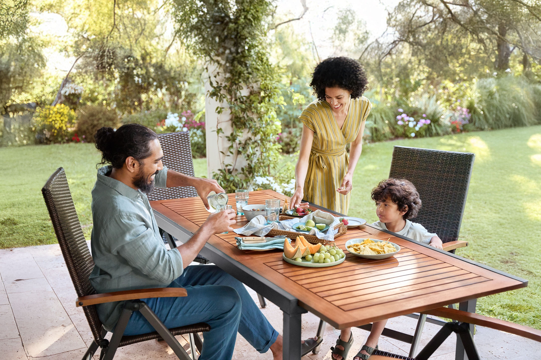 Family dining outdoors with a wooden table and rattan chairs.