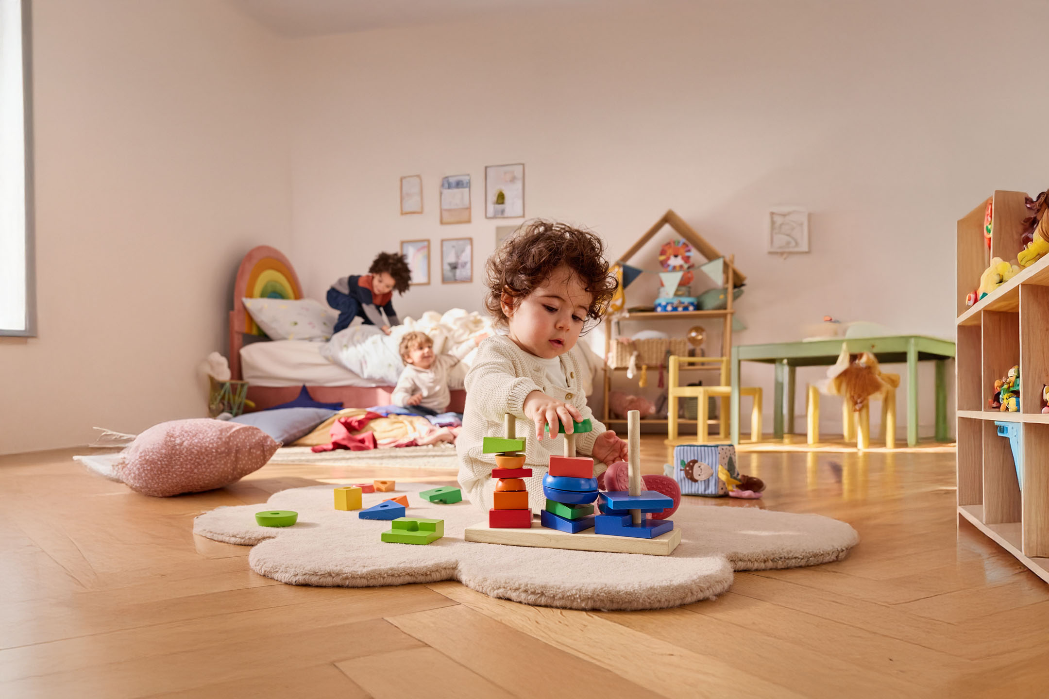 A toddler plays with a wooden stacking toy in their room.