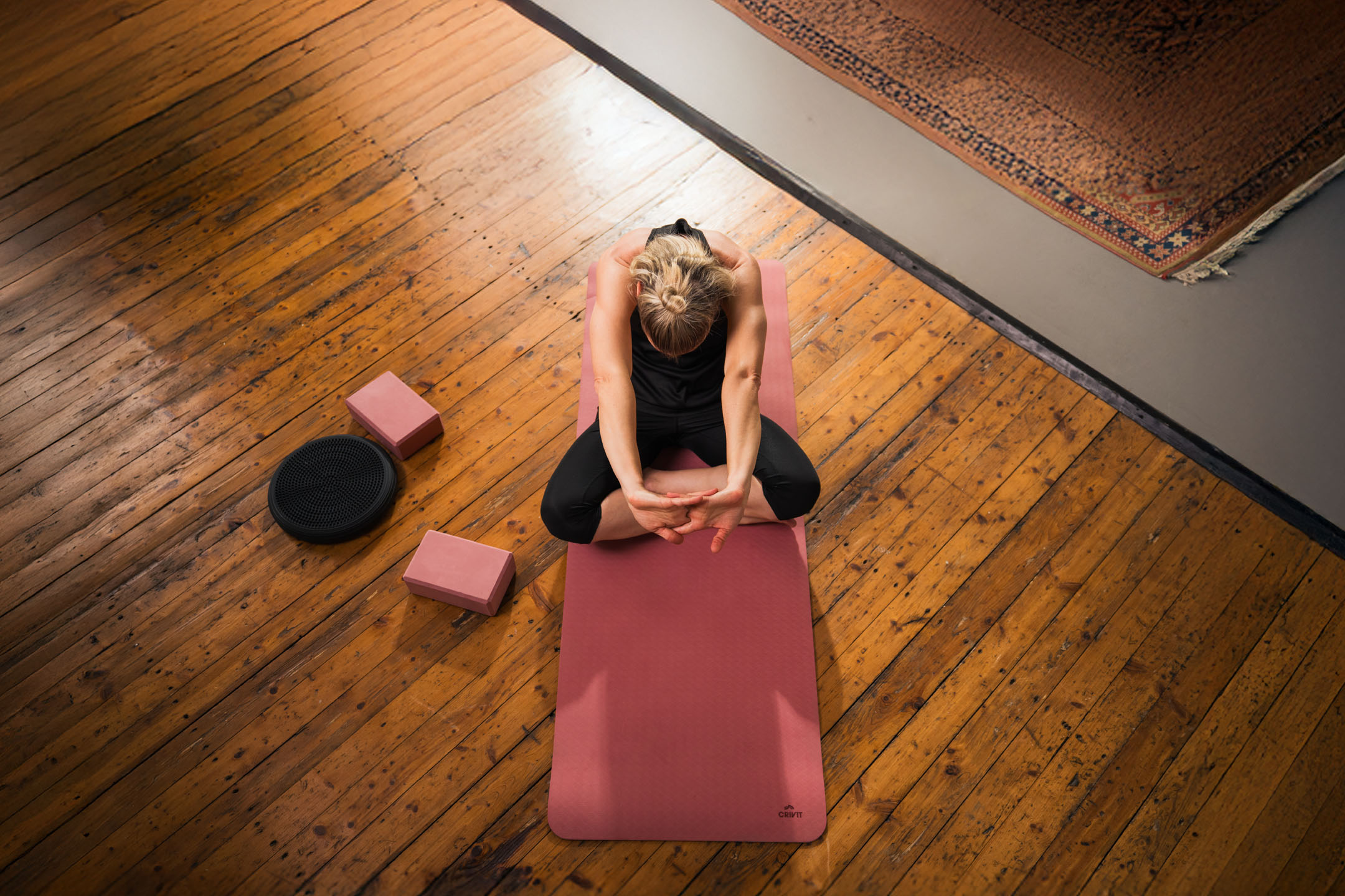 Woman practicing yoga on a pink mat with blocks and a balance disc.