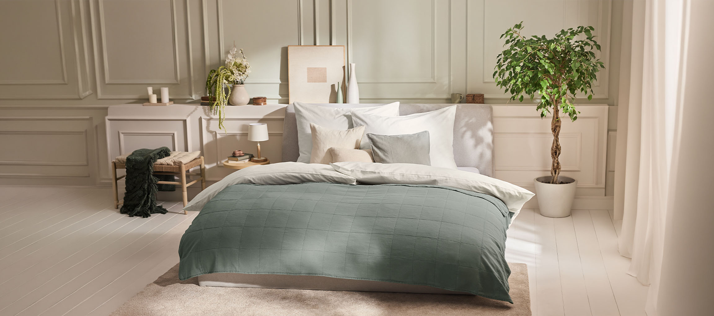 Bedroom with a bed, green duvet, pillows, nightstand, and a plant.
