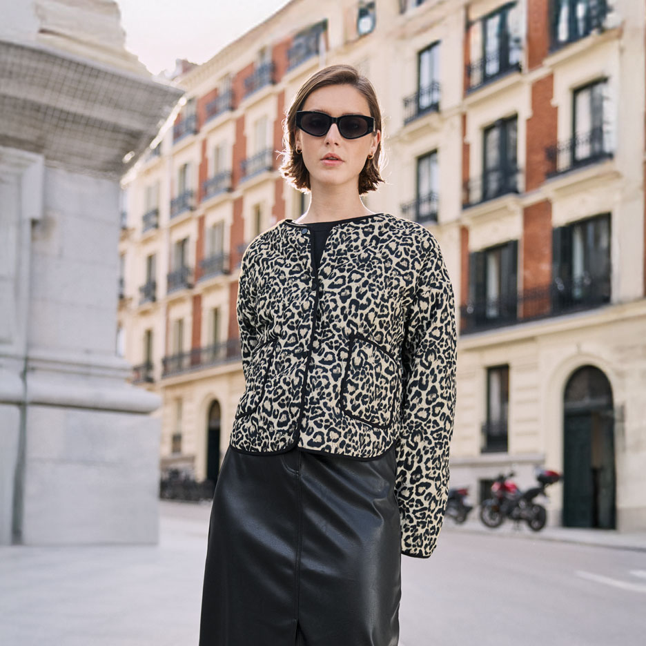 Woman in a leopard print jacket and black skirt, on an urban street.