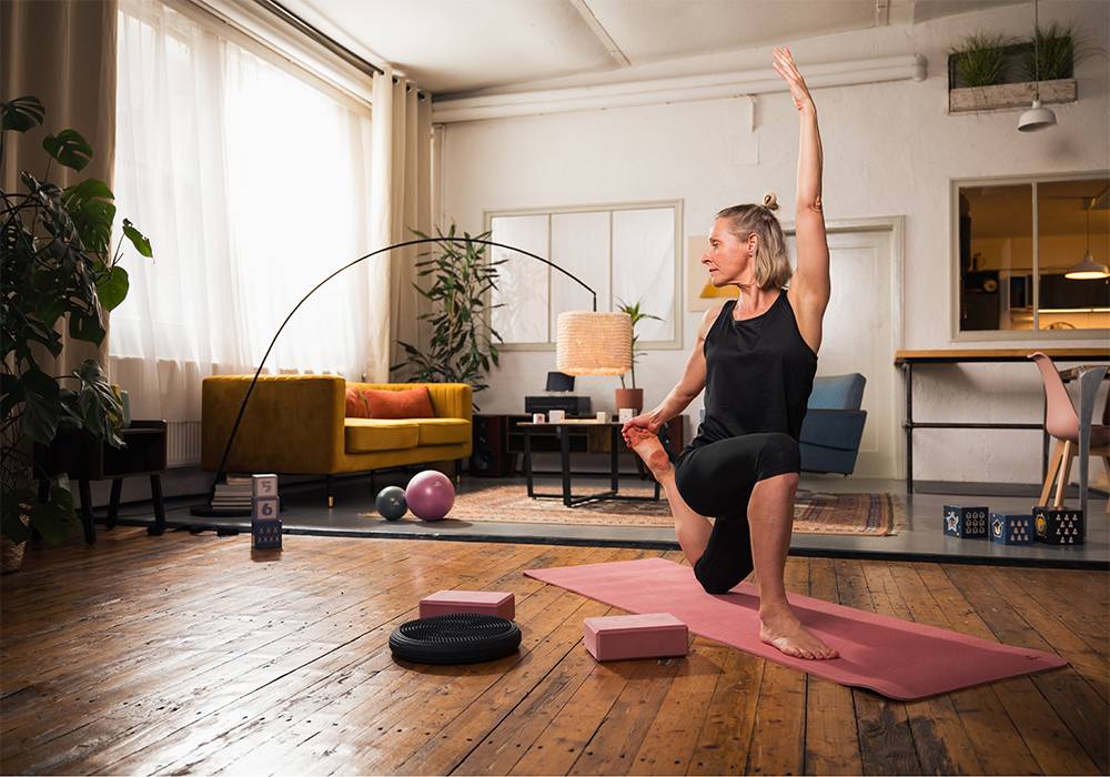 Woman practicing yoga at home with mat, blocks, and balance disc.