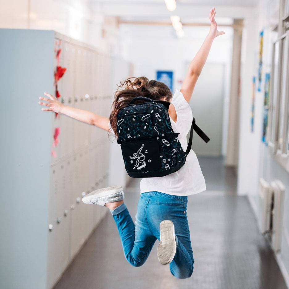Child with backpack jumping in a school hallway.