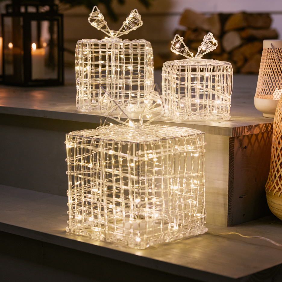 Light-up LED gift boxes on a wooden shelf, with a lantern in the background.