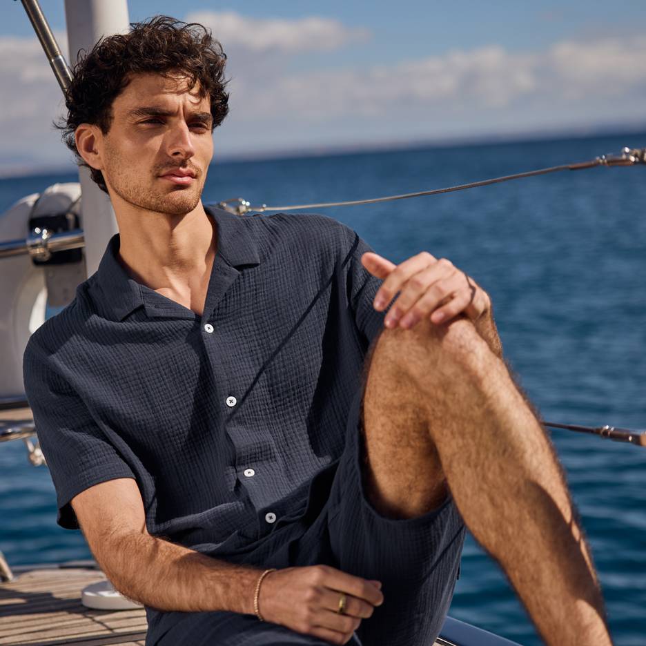 Man in a dark blue shirt and shorts on a yacht, looking out at the sea.